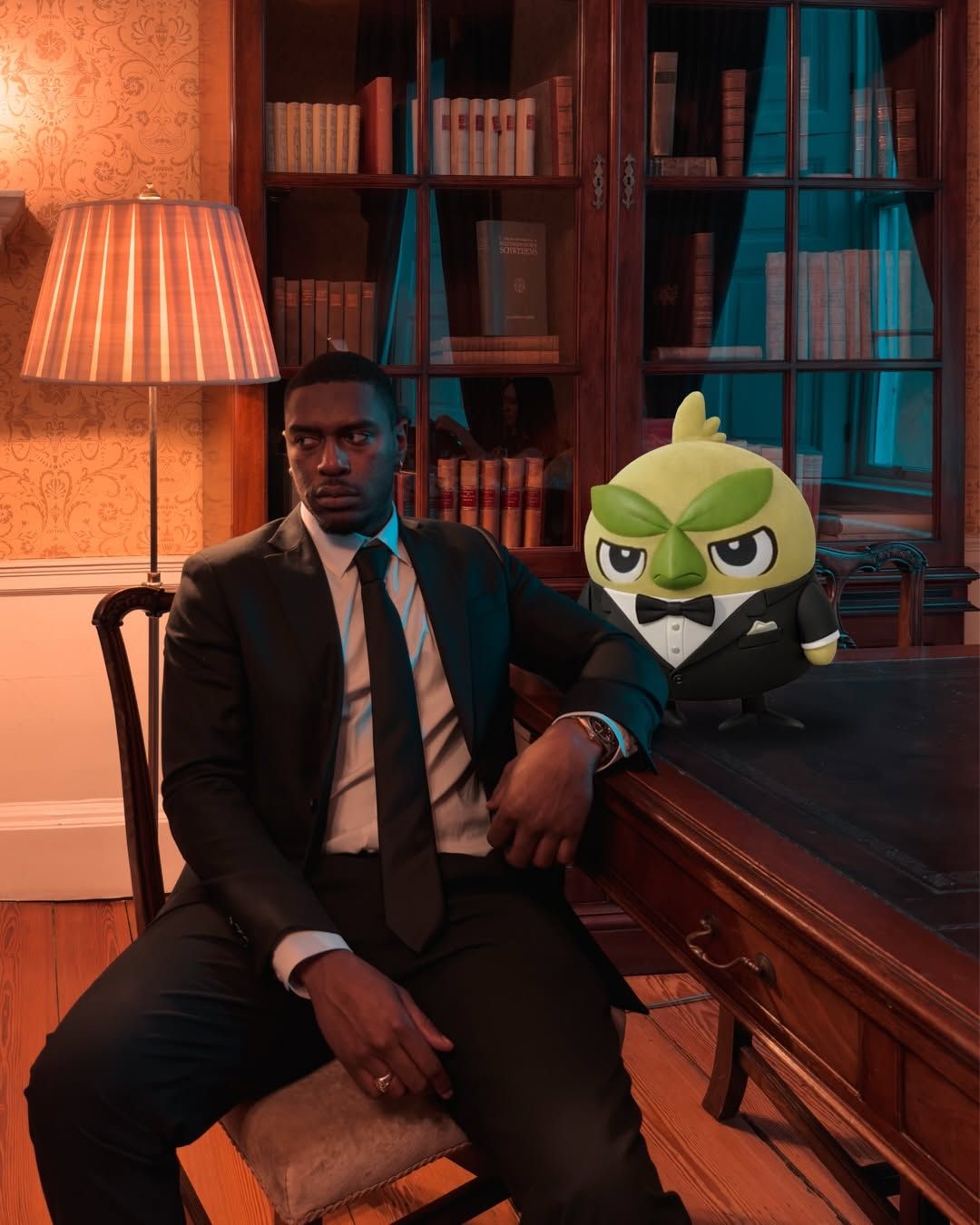 Josiah Campbell in a black suit at an antique desk, next to a Pokémon plush in a tuxedo